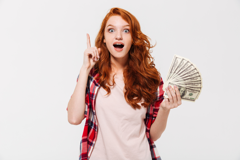 Picture of excited pretty young redhead lady standing isolated over white wall background looking camera while holding money have an idea.