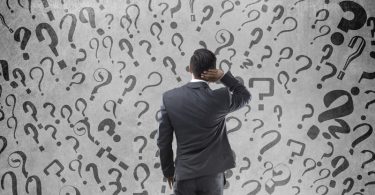 Rear view of confused Indian businessman with question marks on wall